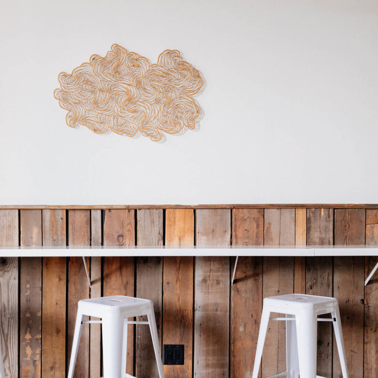 Inside the Fraser Street location of Earnest Ice Cream, wall with cloud art and two stools
