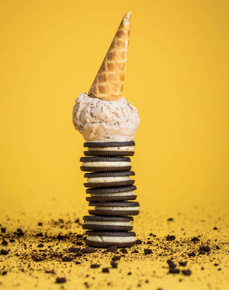 Ice cream cone on top of a stack of cookies and cream sandwiches, on a yellow background.