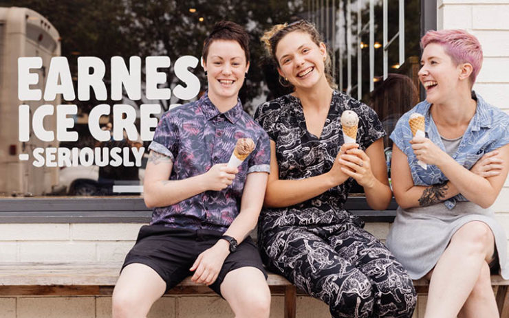 Earnest Ice Cream employees in front of storefront window, sitting and enjoying ice cream cones.
